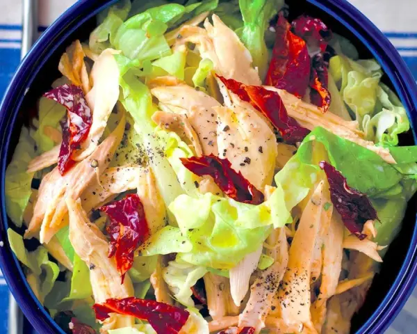 Insalata di pollo lesso con lattuga croccante e pomodori secchi, condita con pepe nero macinato.