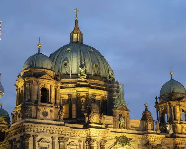 Prachtvolle Kuppeln des Berliner Doms im Abendlicht, mit dem Fernsehturm im Hintergrund. Ein Wahrzeichen der Kirchen in Berlin.