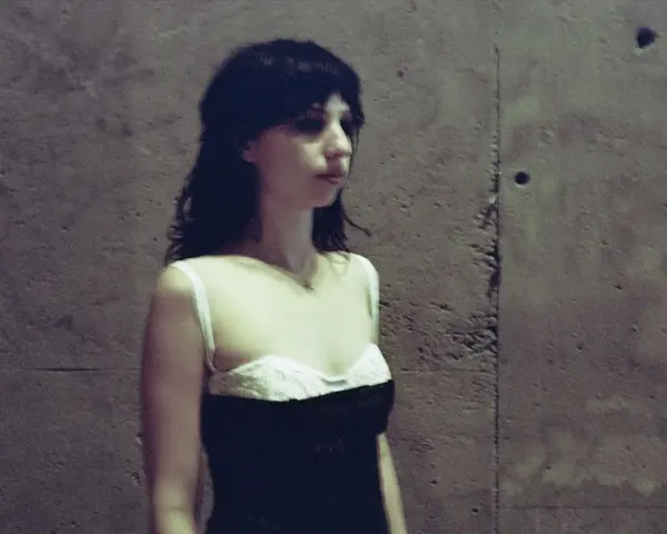 Stella Rose Gahan w czarnej sukience z białym gorsetem, stoi przy betonowej ścianie.