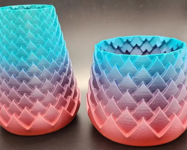 Two dragon-scale patterned vases, created with color 3d printing, showcase a gradient from coral pink to teal blue.