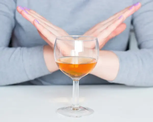 Ręce w geście "stop" nad kieliszkiem z bursztynowym płynem. Pytanie: czy po szczepieniu można pić alkohol? Odpowiedź brzmi: nie.