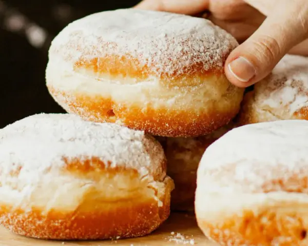 Stos puszystych pączków oprószonych cukrem pudrem. Idealne na tłusty czwartek, te fit pączki kuszą apetycznym wyglądem.