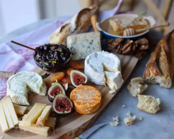Plateau de fromages variés, dont un fromage à pâte cuite, avec figues, confiture et pain.