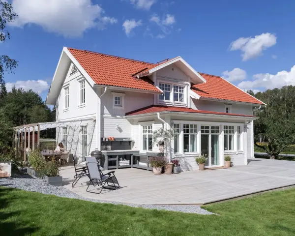 Vitt hus med rött tak och stor altan. Perfekt för att behandla altan och njuta av sommaren.
