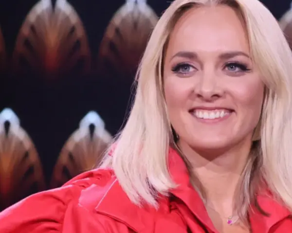 Uśmiechnięta blondynka w czerwonej marynarce, z błękitnymi oczami i delikatnym naszyjnikiem. Ola, jaka to melodia?