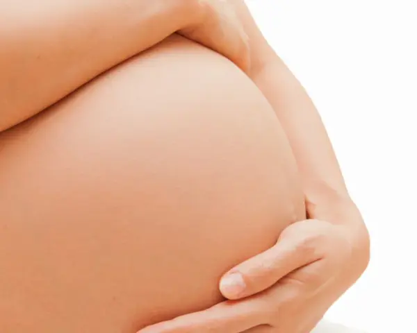 Dłoń obejmuje ciążowy brzuch. Zaparcia w ciąży to częsty problem, ale można sobie z nimi radzić.