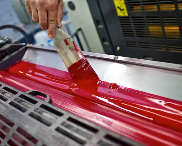 Mano esparciendo tinta roja en rodillos de imprenta, mostrando las ventajas de la imprenta para la difusión masiva de información.
