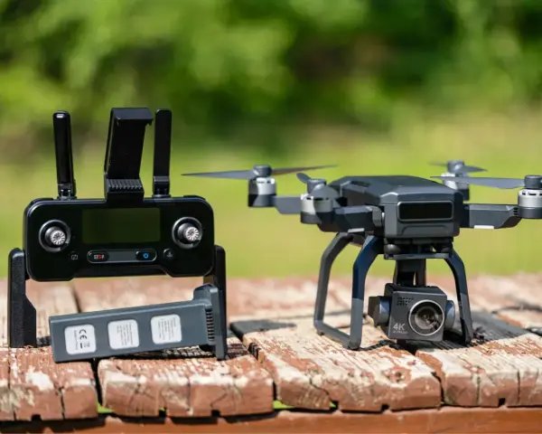 A drone with a 4K camera sits on a wooden table next to its controller and a spare battery, ready for its next follow drone adventure.