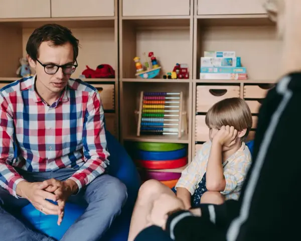 Terapeuta rozmawia z dzieckiem, ćwicząc teorię umysłu. W tle zabawki i pomoce edukacyjne.