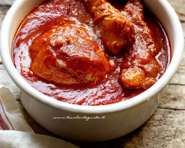 Un saporito ragù napoletano in una ciotola bianca, con pezzi di carne succulenta immersi nel sugo rosso intenso.