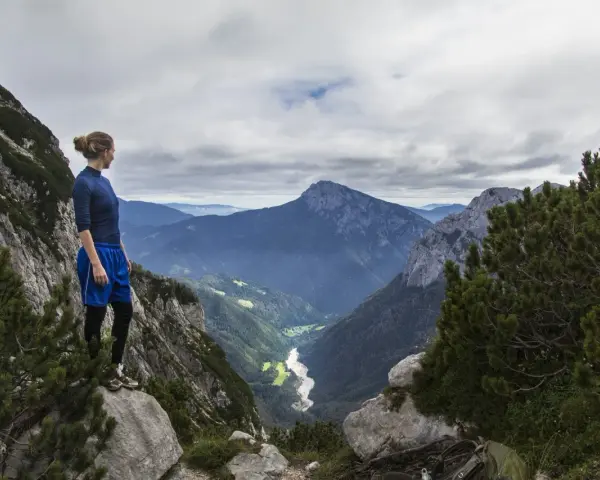 Donna in cima a una montagna, contemplando un vasto paesaggio alpino. Il vero hiking significato è nella libertà e nella vista mozzafiato.