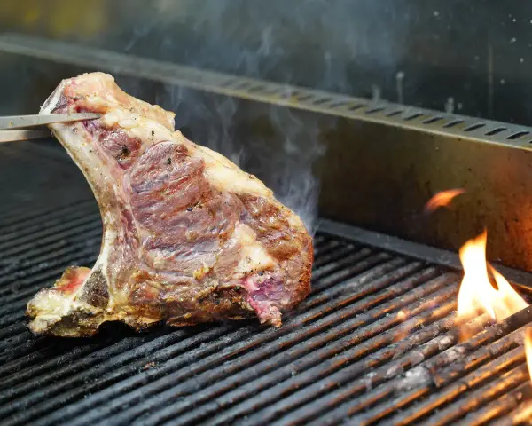 Una succulenta bistecca alla fiorentina, con la sua storia di sapori, cuoce sulla griglia tra fiamme vive e fumo.