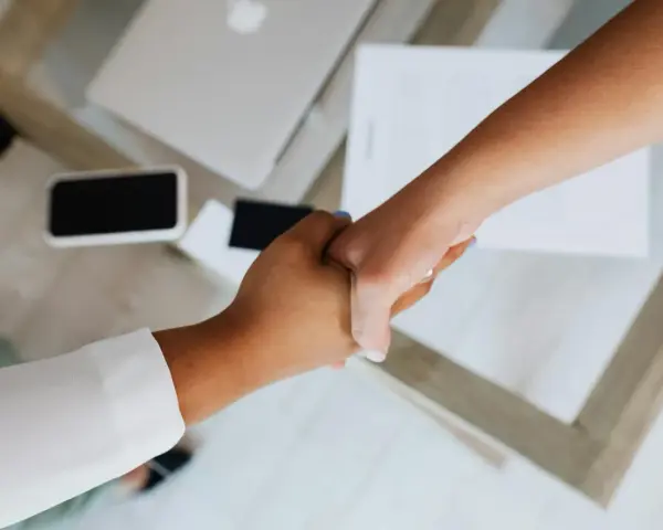Uścisk dłoni symbolizujący podpisanie umowy na czas nieokreślony. Na stole leży laptop i dokumenty.
