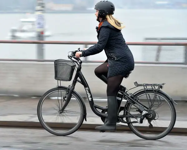 Kvinna cyklar på en elcykel, kanske med bidrag för att underlätta pendlingen. Hon bär hjälm och en varm jacka.