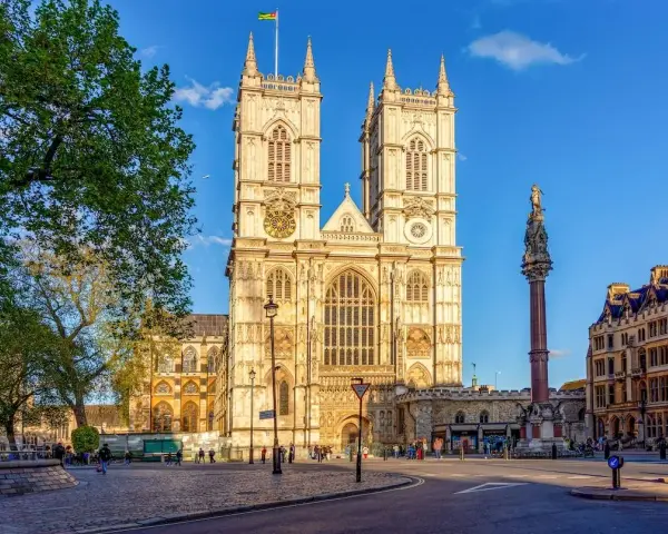 L'abbaye de Westminster, majestueuse et illuminée par le soleil, se dresse fièrement avec ses tours jumelles. Une colonne commémorative se dresse à droite.