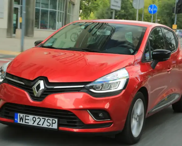 Czerwony Renault Clio 3 1.2 benzyna w ruchu miejskim. Kierowca w okularach przeciwsłonecznych.