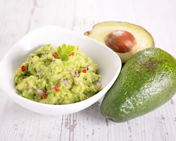 Miseczka guacamole z awokado, cebulą i papryczką chili na drewnianym tle.