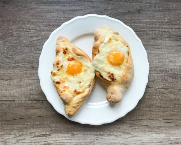 Dwa chaczapuri adżarskie z jajkiem i serem na białym talerzu. Idealne na szybki obiad, gdy masz ochotę na chaczapuri przepis.
