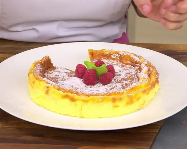 Tarta de queso Arguiñano recién horneada, espolvoreada con azúcar glas y decorada con frambuesas y menta.