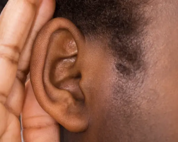Une main couvre une oreille, comme pour mieux entendre ou se protéger du bruit. Cela peut évoquer ce qu'est-ce qui provoque des acouphènes.