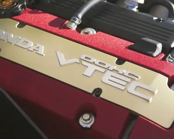 Złota pokrywa silnika Honda z napisem VTEC, otoczona czerwonym, błyszczącym wykończeniem.