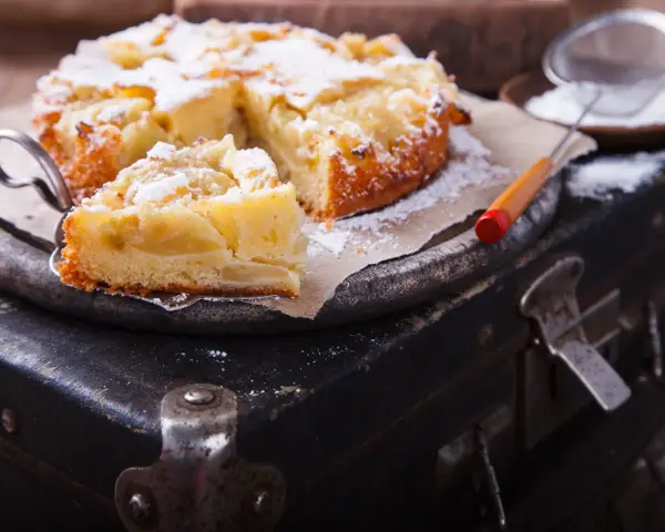 Pyszne, domowe ciasto z jabłkami, posypane cukrem pudrem, czeka na spróbowanie. Idealne na deser!