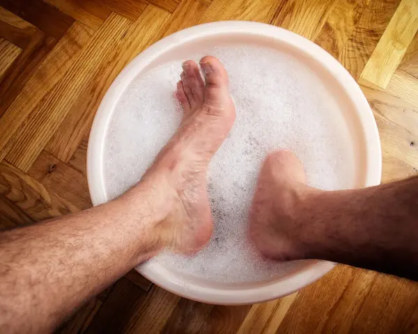 A person's feet soaking in a bubbly foot bath on a wooden floor.
