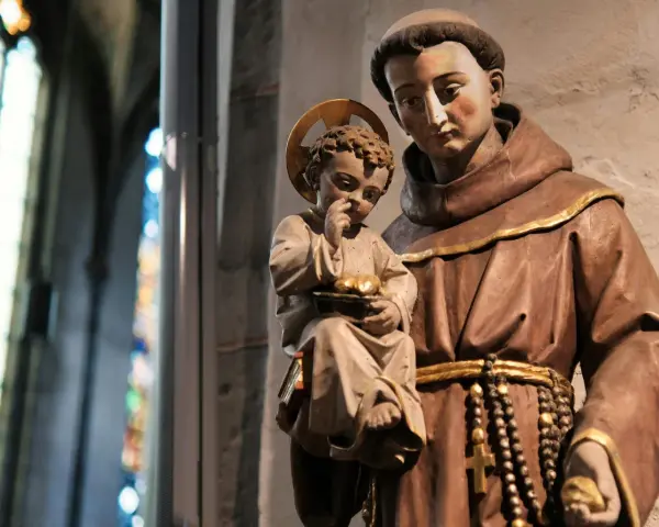 A statue shows what friars wear: brown robes, a cord belt, and a rosary. A child with a halo holds fruit.