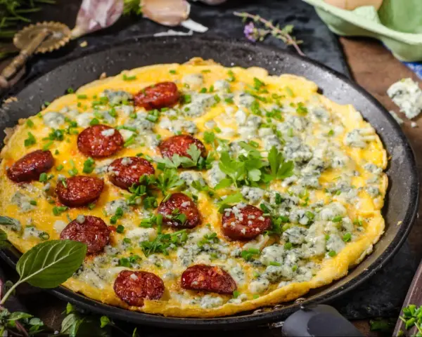 Pyszny omlet na słono z kawałkami chorizo i niebieskim serem, posypany szczypiorkiem i natką pietruszki.