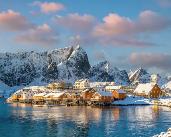 Snow-covered mountains frame a picturesque village with orange and white houses on stilts over the water, a scene from one of Europe's best winter destinations.