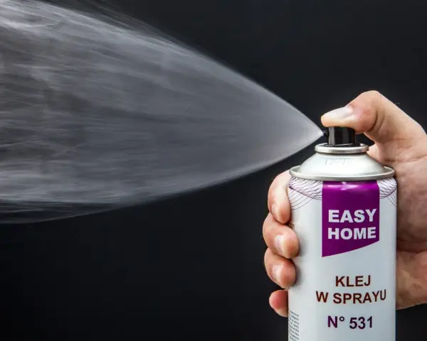 Dłoń trzyma puszkę z klejem w sprayu, który jest rozpylany. Idealny klej do podsufitki bez zdejmowania.