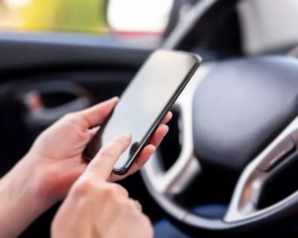 Ręce trzymają smartfon w samochodzie, obok kierownicy. Może to być pomocne, by dowiedzieć się, co to aux i jak podłączyć muzykę.