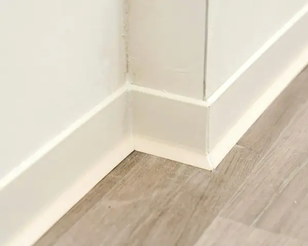 Angolo di una stanza con pavimento in laminato grigio e battiscopa bianco appena posato.
