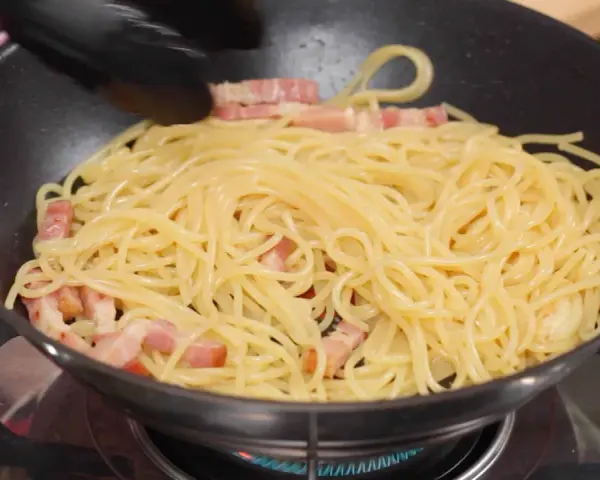 Espaguetis con trozos de panceta en una sartén, preparándose para unos deliciosos tallarines a la carbonara.