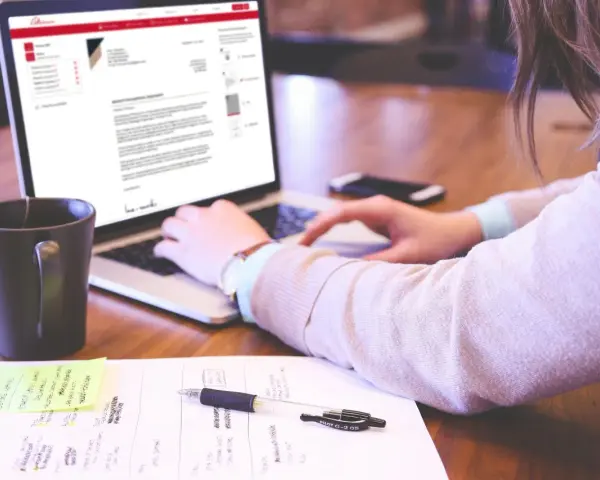 Kobieta pisze list motywacyjny bez doświadczenia na laptopie, obok kubek kawy i notatki.