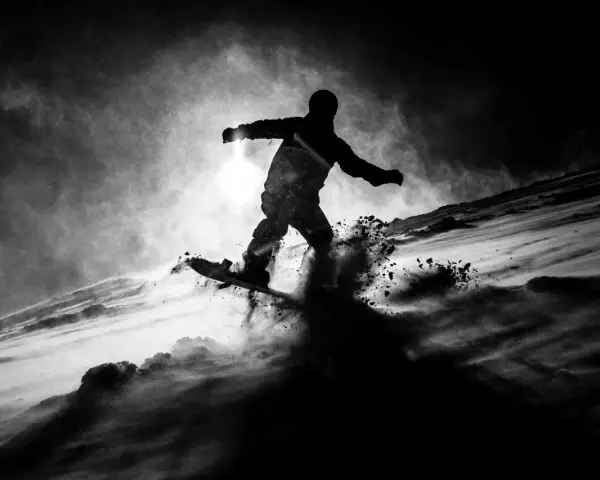 Une silhouette de snowboarder en plein saut, projetant de la neige. L'image, une peinture sur toile noire, capture l'énergie du mouvement dans un style dramatique.