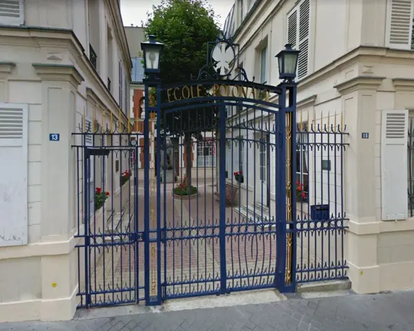 Brama do Ecole de Paris, ozdobiona złotymi detalami, prowadzi na dziedziniec z drzewem i ławką.