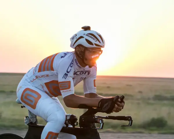 Cyclist in aerodynamic gear races across America at sunset, pushing through the vast landscape.