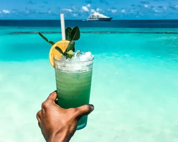 Orzeźwiający drink na plaży z widokiem na turkusowe morze i luksusowy jacht. Idealny moment relaksu.