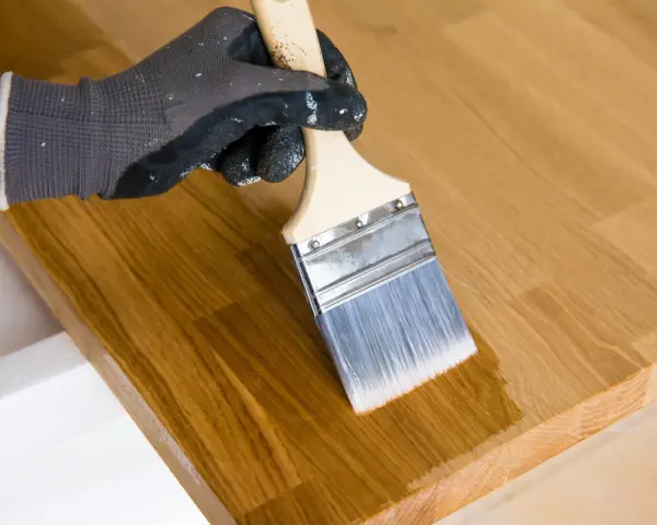 Main tenant avec un pinceau pour enlever l'huile de lin sur du bois.