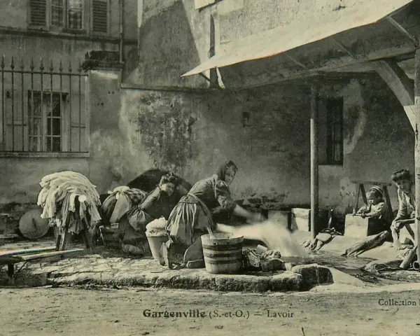 Des femmes s'affairent à laver le linge autrefois, dans une cour. Des enfants observent ce travail pénible.