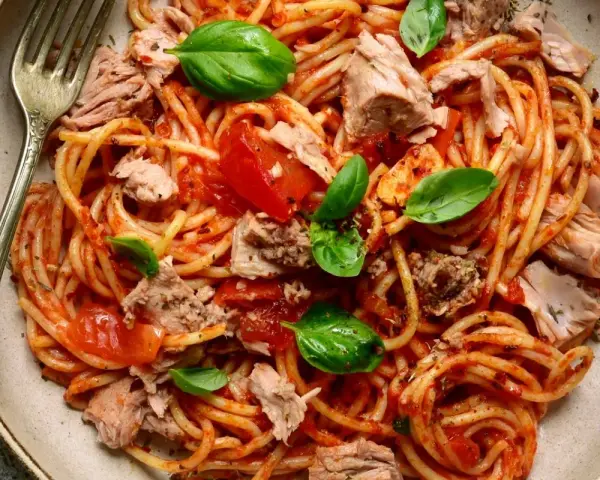 Spaghetti al sugo di pomodoro con abbondante tonno in scatola, guarniti con foglie di basilico fresco. Un piatto semplice e gustoso.