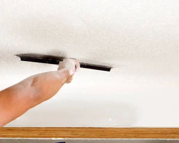 A dusty hand uses a trowel to texture a ceiling, demonstrating how to texture a ceiling for a fresh look.