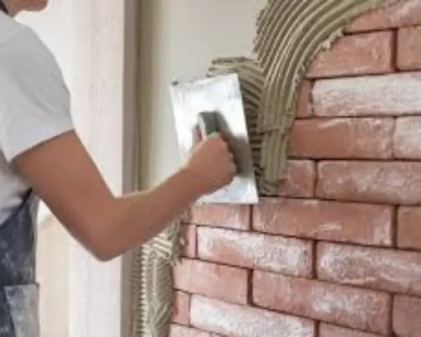 Un ouvrier applique de l'enduit sur une brique avec une truelle, créant une texture rustique.