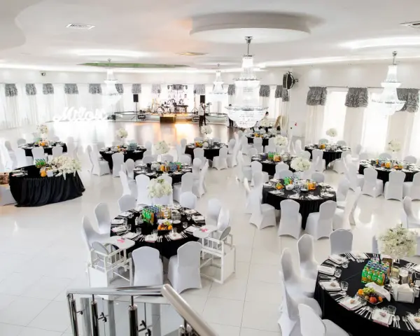 Elegancka sala weselna z czarnymi obrusami i białymi pokrowcami na krzesła. Stoły zastawione, gotowe na przyjęcie gości. Zastanawiasz się, ile za talerzyk na weselu?