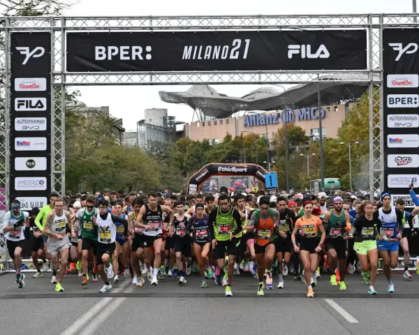 Corredores listos para la media maratón Milán 2021. La carrera arranca bajo un arco con patrocinadores y el logo de Fila.