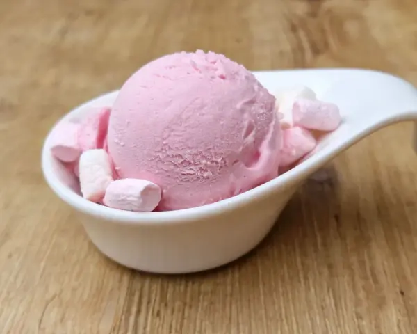 Eine Kugel rosa Bubble Gum Eiscreme mit Marshmallows in einer weißen Schale auf Holzhintergrund.