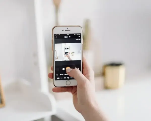 Dłoń trzyma smartfon, na ekranie którego widać aplikację do robienia zdjęć. To jakby snapbridge po polsku, ułatwiający dzielenie się wspomnieniami.