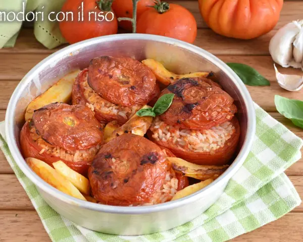 Pomodori ripieni di riso, cotti al forno con patate e basilico. Un piatto estivo saporito e colorato.