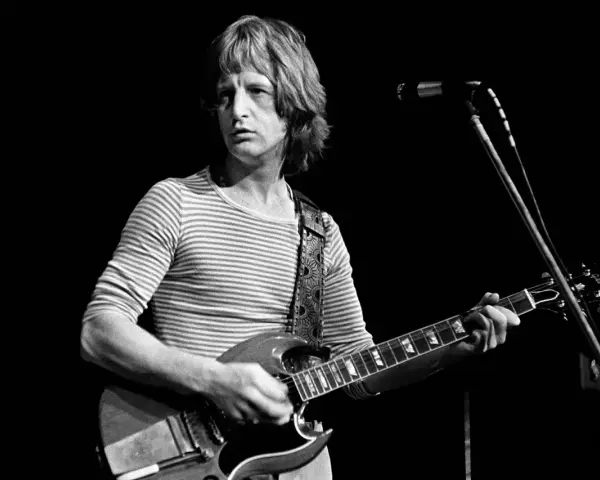 Pete Ham, mit gestreiftem Shirt und Gitarre, blickt konzentriert auf die Bühne.